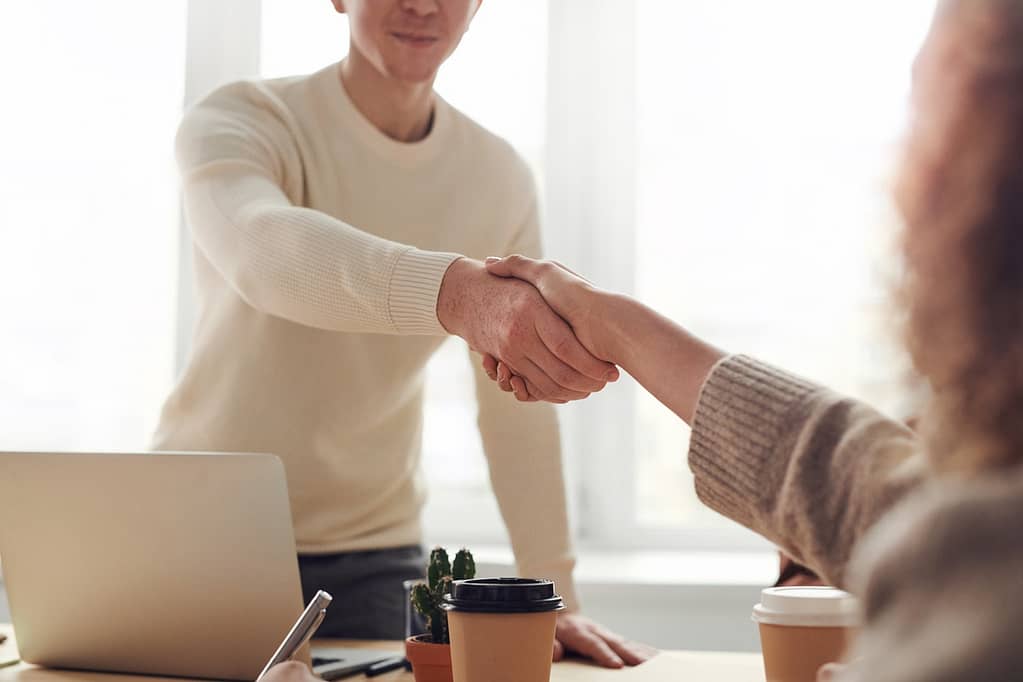 A handshake over an pen laptop and disposable coffee cups